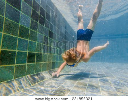 A Child Boy Is Swimming Underwater In A Pool, Smiling And Holding Breath, With Swimming Glasses.