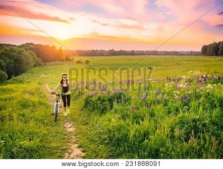Young Sporty Woman Riding A Bicycle At Sunset. Sporty Girl Goin Uphill On Bike Among The Field Of Lu
