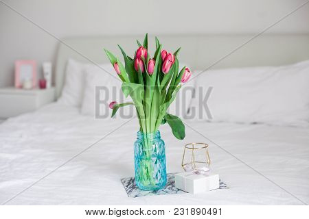 Home Interior. Bedroom. A Bouquet Of Tulips In A Glass Vase, A Candle, A Tray, A Box With A Gift Sta