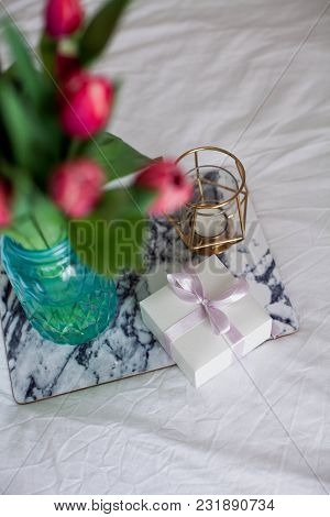 Home Interior. Bedroom. A Bouquet Of Tulips In A Glass Vase, A Candle, A Tray, A Box With A Gift Sta