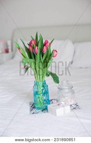 Home Interior. Bedroom. A Bouquet Of Tulips In A Glass Vase, A Candle, A Tray, A Box With A Gift Sta