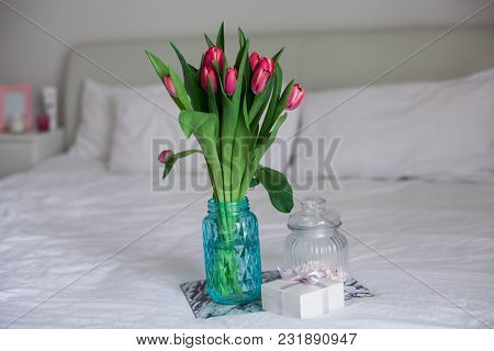 Home Interior. Bedroom. A Bouquet Of Tulips In A Glass Vase, A Candle, A Tray, A Box With A Gift Sta