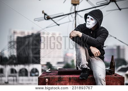Mystery Man In White Mask With Hoody Jacket, Sitting And Hugs His Knees Up With Broken Empty Bottle.