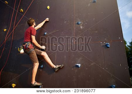 Sporty Man Practicing Rock Climbing In Climbing Gym Artificial Rock Training Wall Outdoors. Young Ta