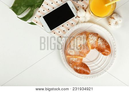 Composition with fresh tasty crescent roll and mobile phone on white background