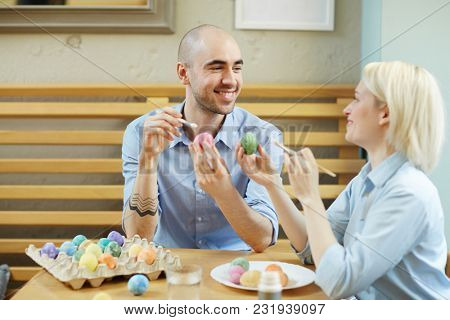 Young couple discussing how they going to celebrate Easter while painting eggs