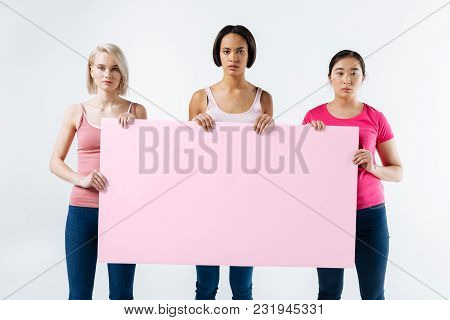 Social Activists. Serious Pleasant Young Women Standing Against White Background And Looking At You 