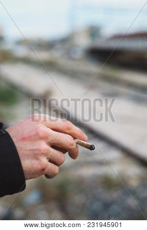 closeup of a young caucasian man outdoors smoking a hand-rolled cigarette or a joint
