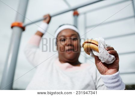 Hamburger in plump hand of young female exercising on sports facilities outdoors