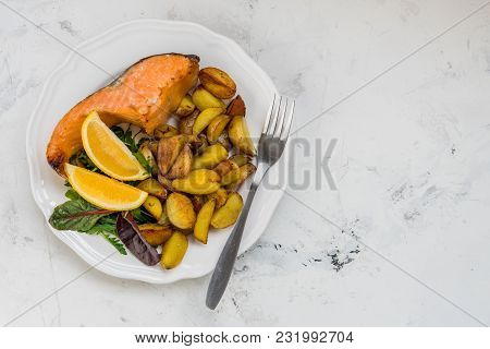Fried Potatoes With Fish And Green Salad On A White Plate