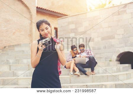 Young Pretty Hipster Teenager Standing And Smiling To Camera With Blurred Of Teenger Sitting On Stai