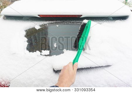 Man Cleaning Car From Snow With Brush. Snow-covered Car Windshield. Parked Car Covered With Snow Dur