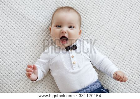 Adorable Baby Boy In White Sunny Bedroom Plays Alone Lying  On The Bed.charming Beautiful Lovely Sma