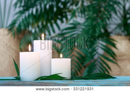 Three White Burning Candles On Palm Background