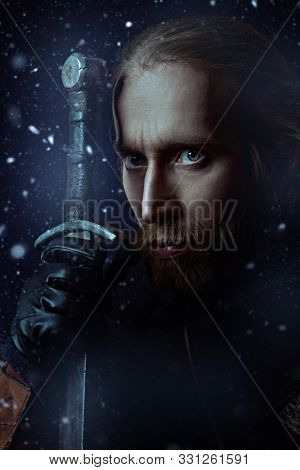 Close-up portrait of a medieval knight in armour and with a sword over winter background. Historical reenactment. 