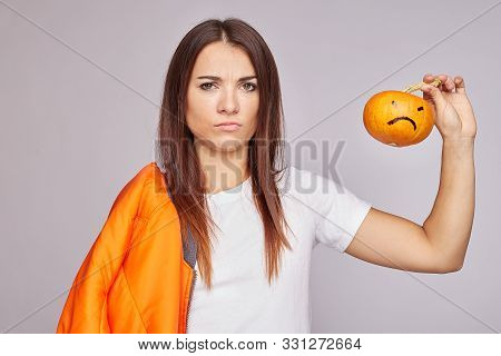 Indoor Shot Of Confused Displeased Woman, Holds Very Small Pumpkin, Has Puzzed Look, Smirks Face, We