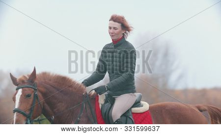 A Woman With Orange Short Hair On A Horse Back
