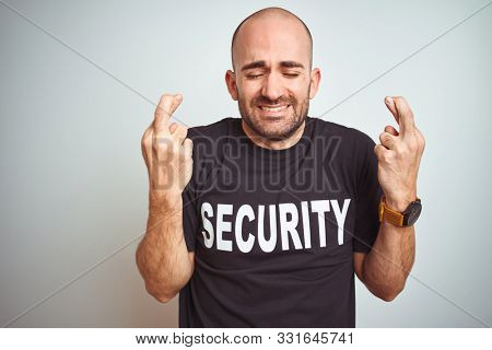 Young safeguard man wearing security uniform over isolated background gesturing finger crossed smiling with hope and eyes closed. Luck and superstitious concept.