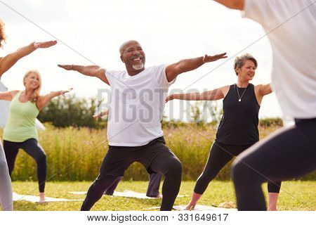 Female Teacher Leading Group Of Mature Men And Women In Class At Outdoor Yoga Retreat