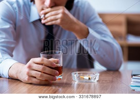 Male employee drinking alcohol and smoking cigarettes at workpla