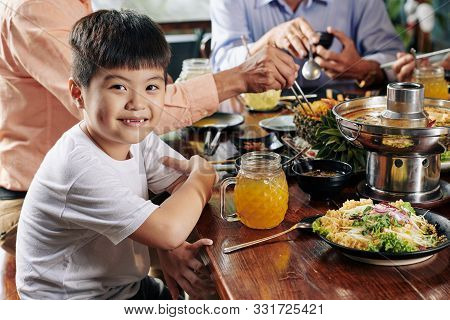 Portrait Of Smiling Little Asian Boy Eating Tasty Dishes Of Vietnamese Cousine At Family Dinner