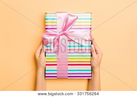 Flat Lay Of Woman Hands Holding Gift Wrapped And Decorated With Bow On Gold Background With Copy Spa