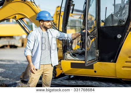 Portrait Of A Handsome Builder Standing Near The Escavator On The Open Ground Of The Shop With Heavy