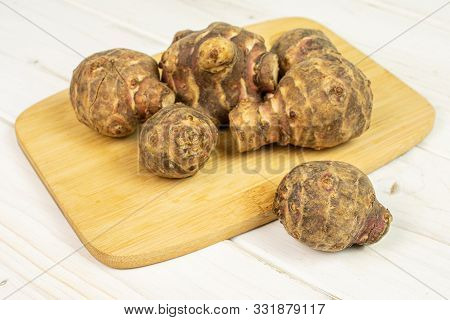 Group Of Six Whole Fresh Brown Jerusalem Artichoke On Bamboo Cutting Board On White Wood