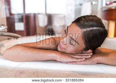 Woman relaxing in bathtub at home taking hot bath wellness alone time. Asian lady happy sleeping in luxury spa hotel room lifestyle.