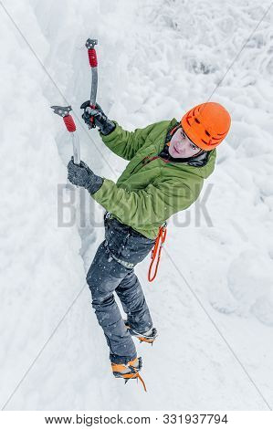 Alpinist Man With Ice Tools Axe In Orange Helmet Climbing A Large Wall Of Ice. Outdoor Sports Portra