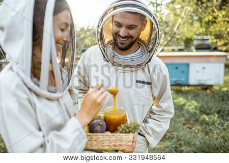 Beekepers In Protective Uniform Standing With Fruits And Honey In The Jar, Tasting Fresh Product On 