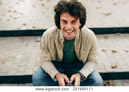 Portrait Of Smiling Young Man Standing Outdoors, Typing Messages On Mobile Phone. Young Male With Cu
