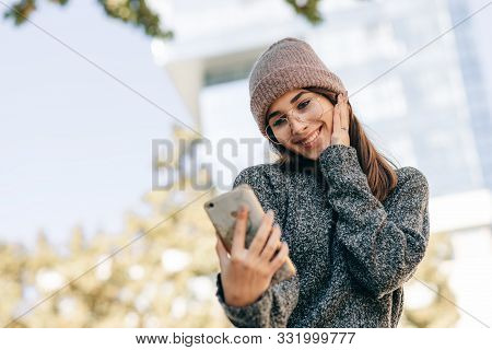 Outdoor Portrait Of Beautiful Young Woman Standing Against Building's Wall And Taking Self Portrait 