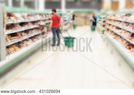 Blurred Aisle And Shelves In Supermarket With Customers. Refrigerator With Meat Products And Sousage