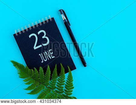 June 23th. Day 23 Of Month, Calendar Date. Black Notepad Sheet, Pen, Fern Twig, On A Blue Background