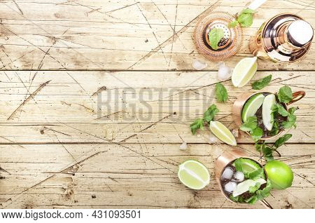 Moscow Mule Cocktails In Copper Mug With Lime, Ice, Ginger Beer, Vodka And Mint. Wooden Background, 