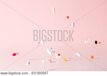 Various colorful pills dropped from top. Medicines jumped on table. Pink background. Selective focus