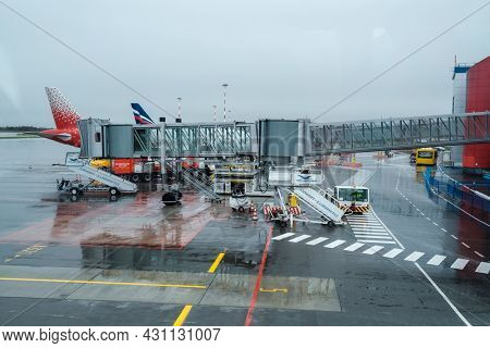 Kaliningrad, Russian Federation - April 25, 2021: Modern jetway and aircraft located on wet asphalt airfield against gray sky on rainy day
