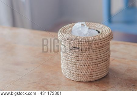 A Light Brown Wicker Basket With White Tissue Paper Inside And Placed On A Light Brown Wooden Table.