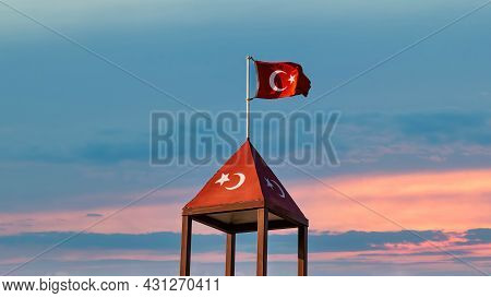 Turkish Flag Over A Top Of Turkish Flag Painted Structure, Waving At Sunset Sky.