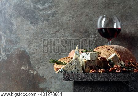 Blue Cheese And Red Wine On An Old Stone Table. Cheese With Walnuts, Bread, And Rosemary. Copy Space