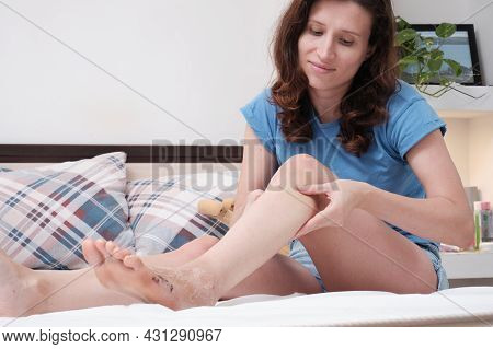 A Woman Sitting On The Bed Massages Her Leg After A Fracture. Home Rehabilitation After Injury. Mass