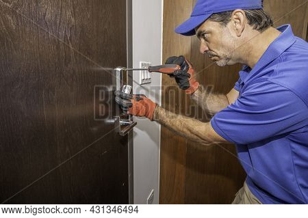 Locksmith Using A Screwdriver On A Deadbolt Lock, Side View, Wearing Uniform And Safety Gloves