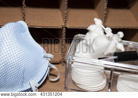Two Blue N-95 Masks And A Plastic Box Of Makeup Rounds, Cotton Balls, And Cotton Swabs In Front Of A