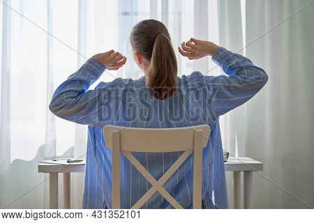 Back View Of Young Female Sitting At Desk And Stretching. Remote Work Challenges And Negative Aspetc