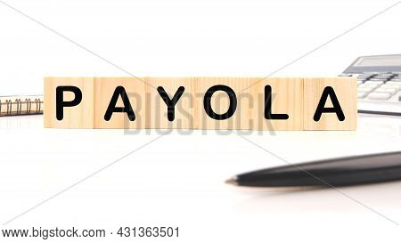 The Inscription Payola On Wooden Cubes On A White Background Next To A Calculator, Pen And Notepad. 