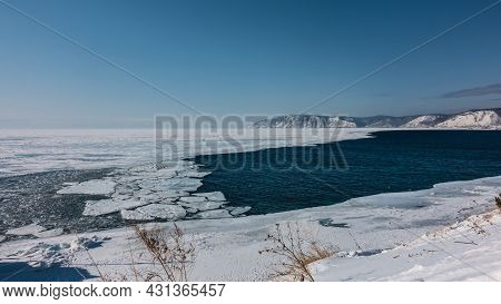 A Non-freezing River Flows Out Of A Frozen Lake. Blue Water And White Ice. Ice Floes Float On The Su