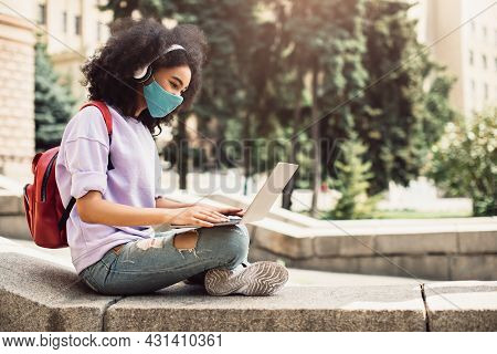African Student Girl Learning Online Using Laptop Wearing Mask Outdoors