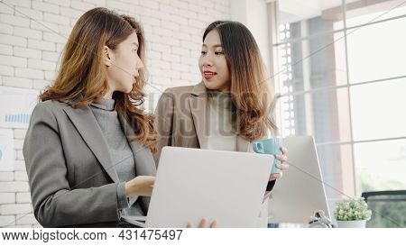 Two Asian Young Creative Businesswomen Holding A Cup Of Coffee, Working On Laptop And Disscuss About