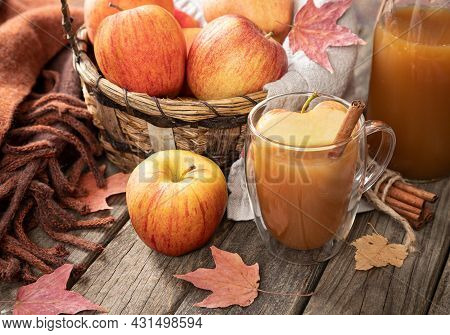 Cup Of Apple Cider And Fresh Apples With Blanket And Autumn Leaves On A Rustic Wooden Table